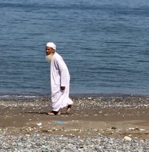Man walks along littered beach in Oman